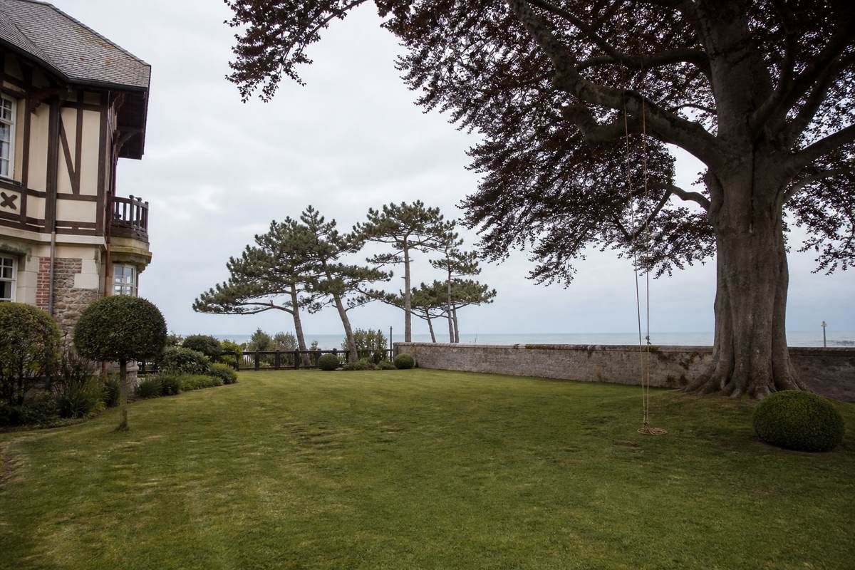 Jardin d'une villa Belle Époque à colombages à Deauville, pins maritimes déformés par le vent et hêtre pourpre, la mer en arrière-plan