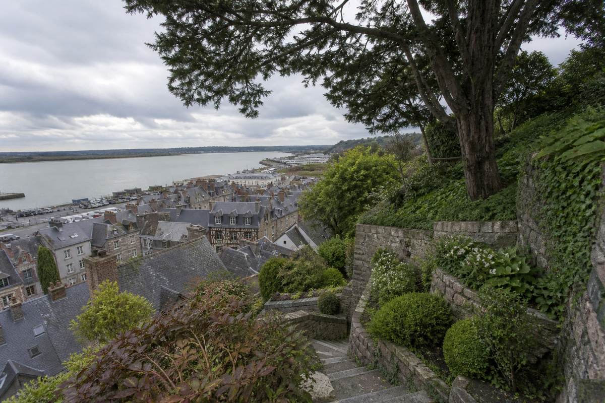 Jardin en terrasse sur le coteau de Honfleur, arbres sur forte pente et murs de soutènement, toits d'ardoise et estuaire de la Seine en contrebas